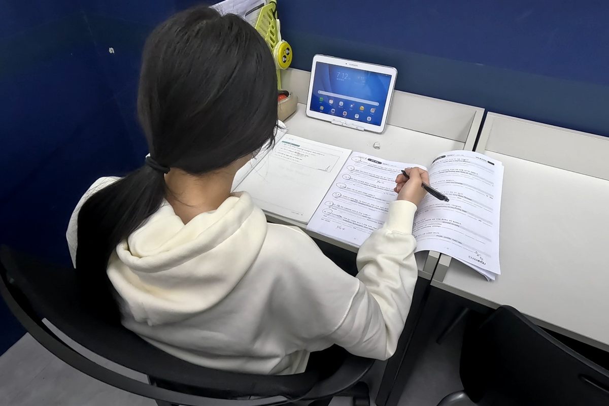 태블릿을 옆에 두고 문제집에 필기하는 학생의 뒷모습