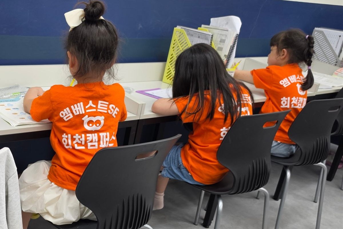 오렌지 티셔츠를 입은 초등학생들이 나란히 앉아 공부하는 뒷모습